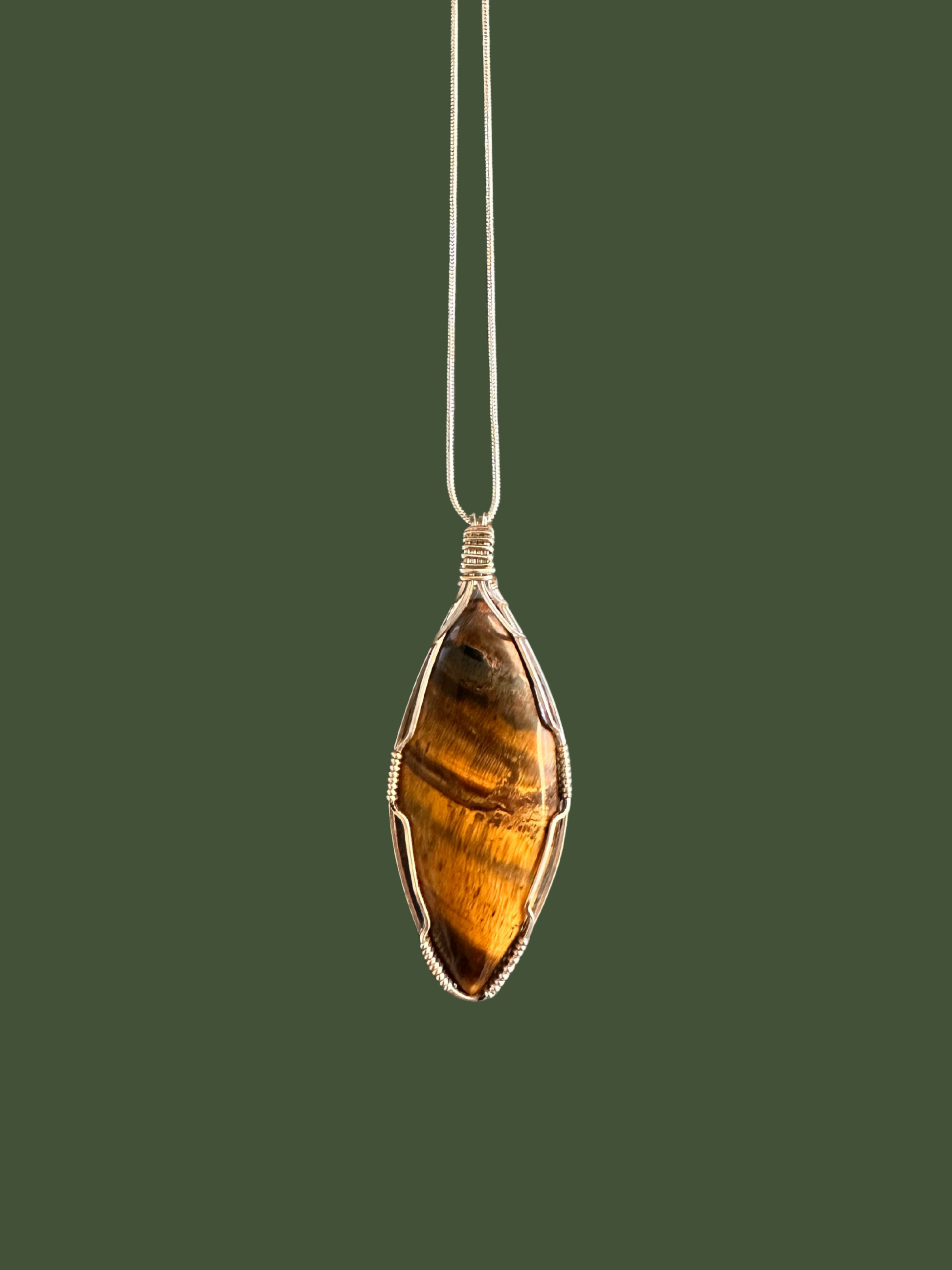 Tiger's eye pendant, tear drop shape, on a silver chain against a green background